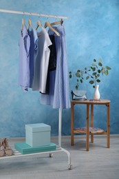 Rack with stylish clothes near light blue wall indoors