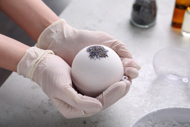 Photo of Woman in gloves with self made bath bomb at grey table, closeup