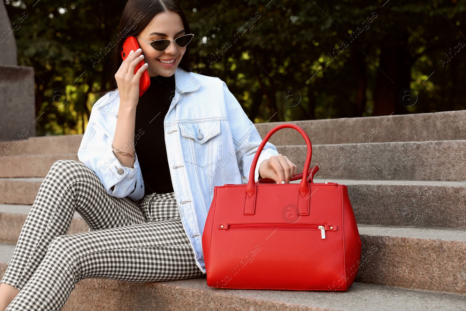 Photo of Young woman with stylish bag talking on phone outdoors