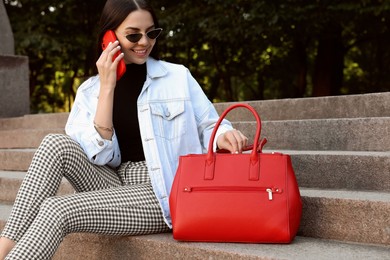 Photo of Young woman with stylish bag talking on phone outdoors