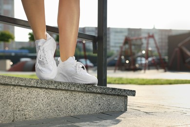 Woman wearing stylish sneakers near railing outdoors, closeup. Space for text