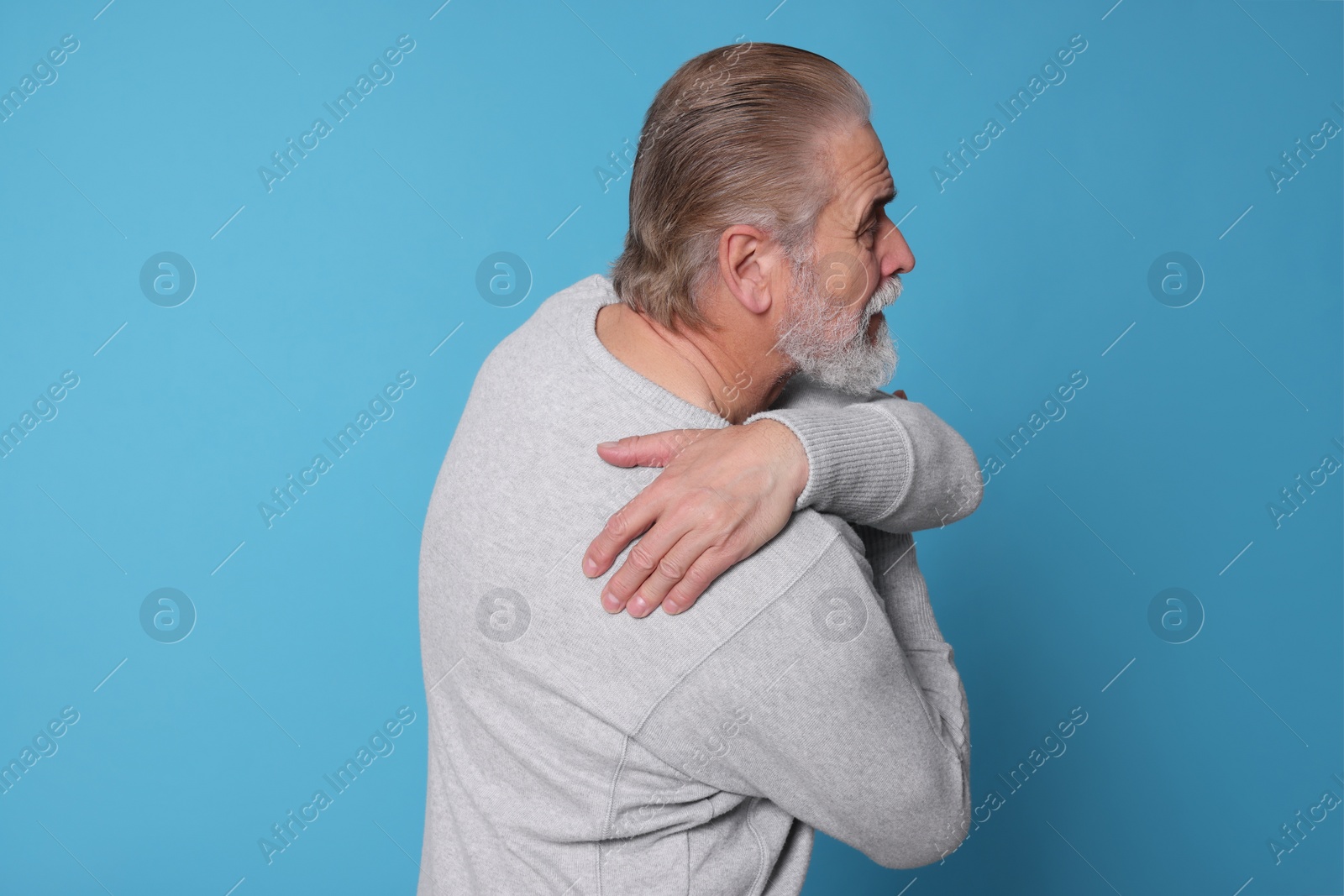 Photo of Senior man suffering from pain in back on light blue background. Arthritis symptoms