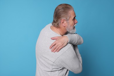 Senior man suffering from pain in back on light blue background. Arthritis symptoms