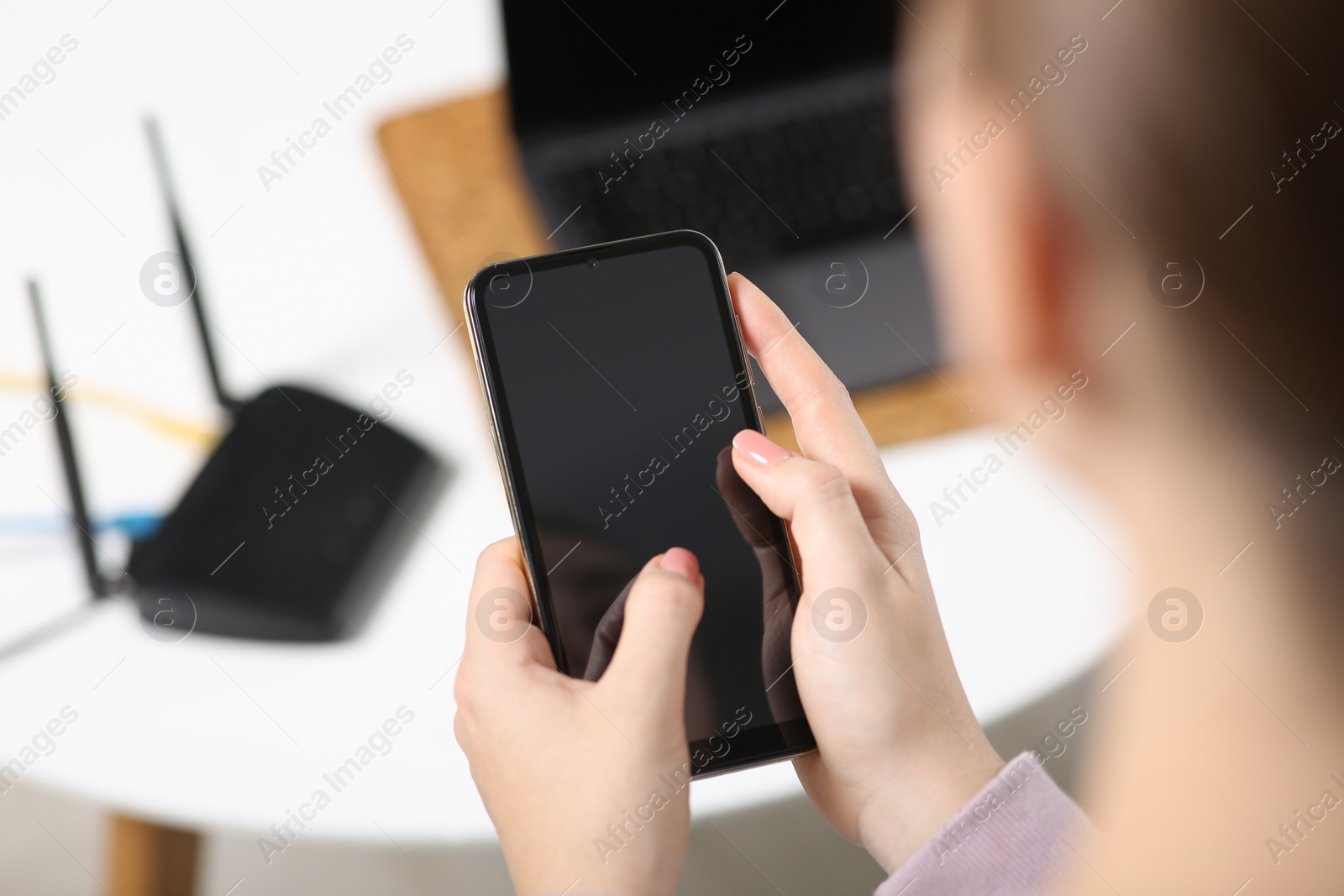 Photo of Woman with smartphone connecting to internet via Wi-Fi router indoors, closeup