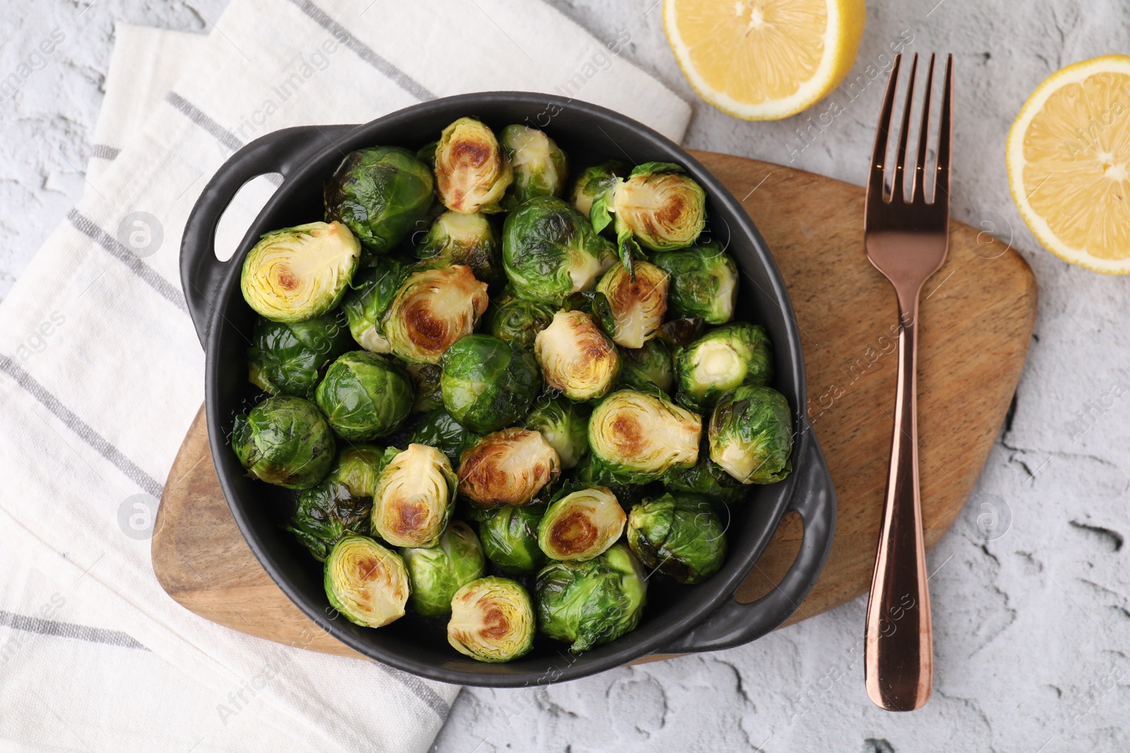 Photo of Delicious roasted Brussels sprouts in baking dish, lemon and fork on white textured table, top view