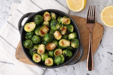 Photo of Delicious roasted Brussels sprouts in baking dish, lemon and fork on white textured table, top view