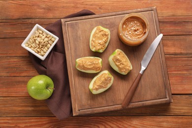 Photo of Slices of fresh apple with nut butter and peanuts on wooden table, flat lay