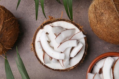 Coconut pieces in nut shell on brown table, flat lay