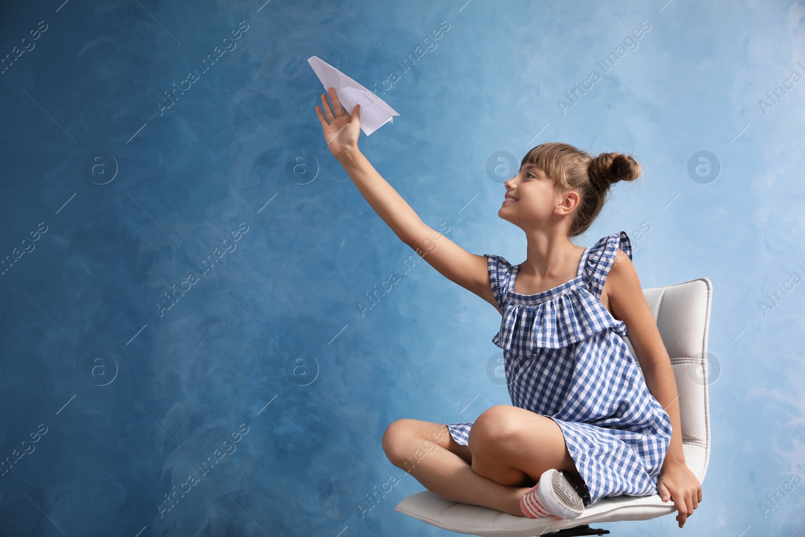 Photo of Cute little girl playing with paper plane on light blue background. Space for text