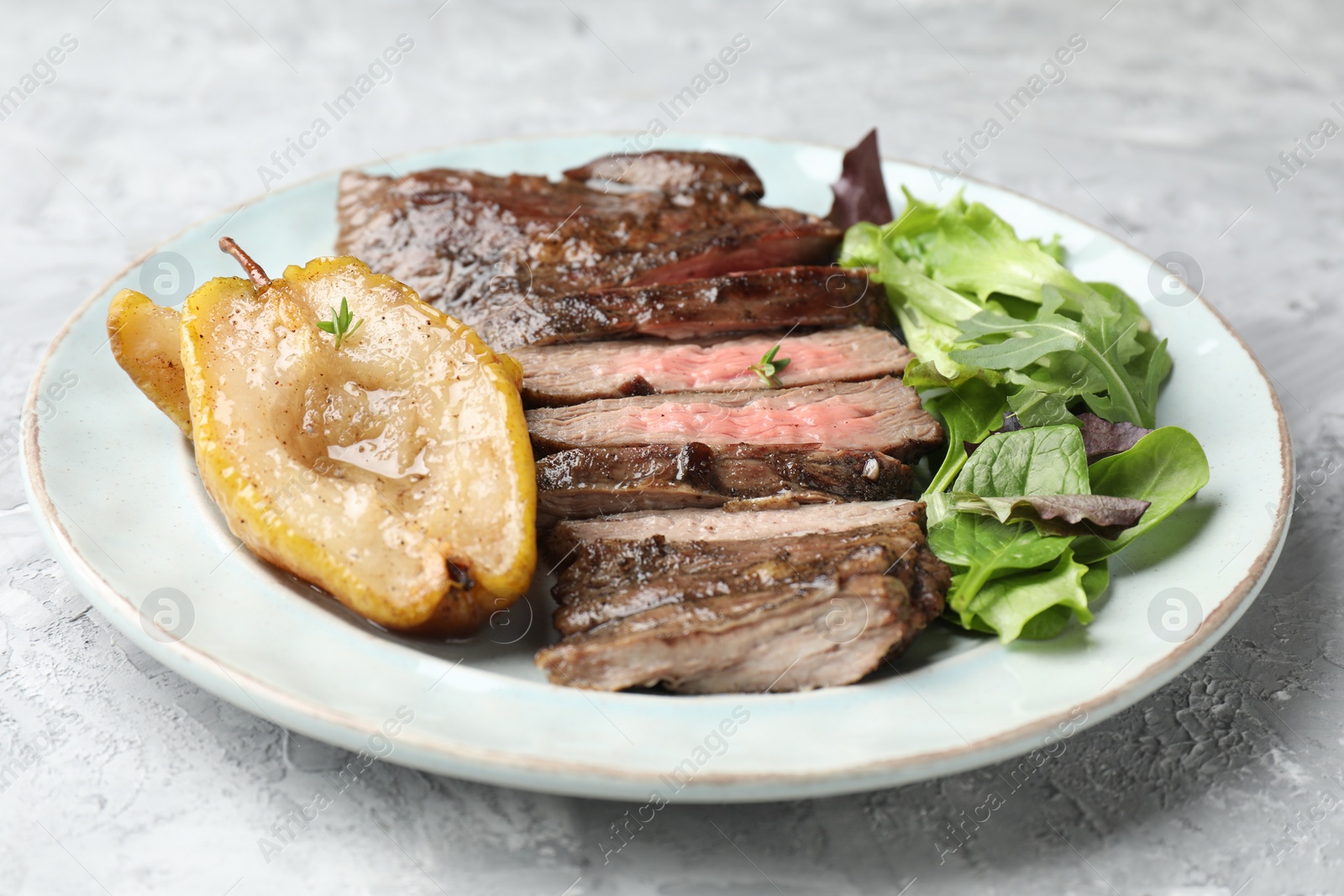 Photo of Pieces of delicious roasted beef meat, caramelized pear and greens on light textured table, closeup