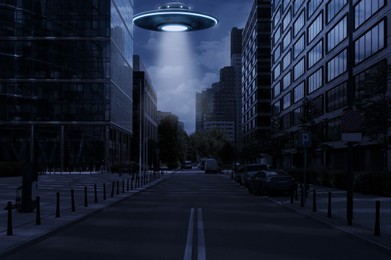 Image of Alien spaceship emitting light over buildings in city. UFO, extraterrestrial visitors