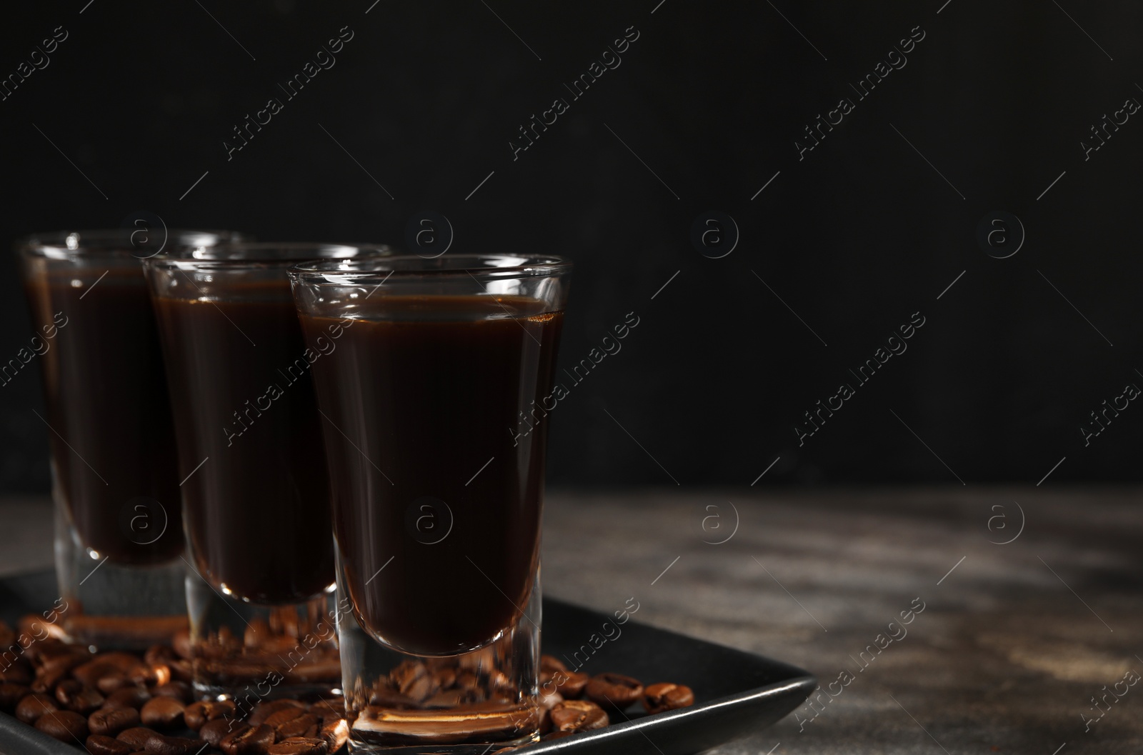 Photo of Shot glasses with coffee liqueur and beans on grey table, closeup. Space for text