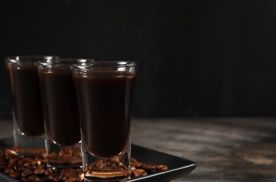 Shot glasses with coffee liqueur and beans on grey table, closeup. Space for text