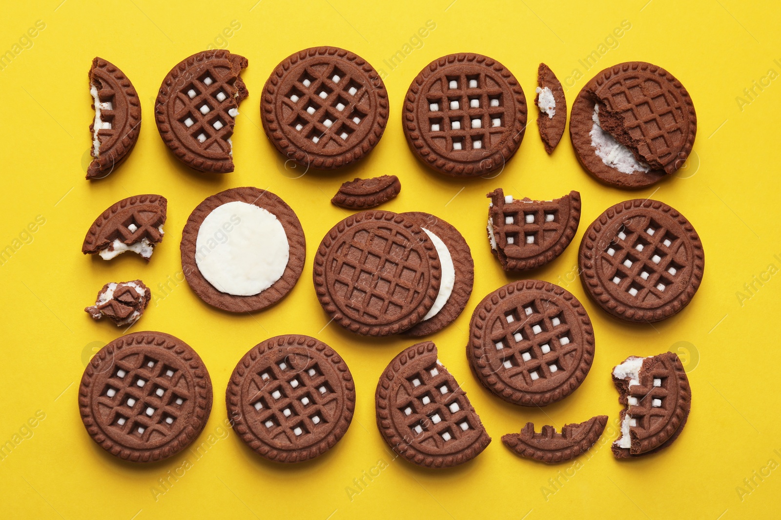Photo of Tasty chocolate sandwich cookies with cream on yellow background, flat lay