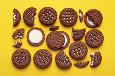 Tasty chocolate sandwich cookies with cream on yellow background, flat lay