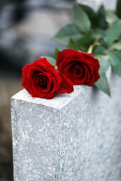 Photo of Red roses on light grey tombstone outdoors. Funeral ceremony