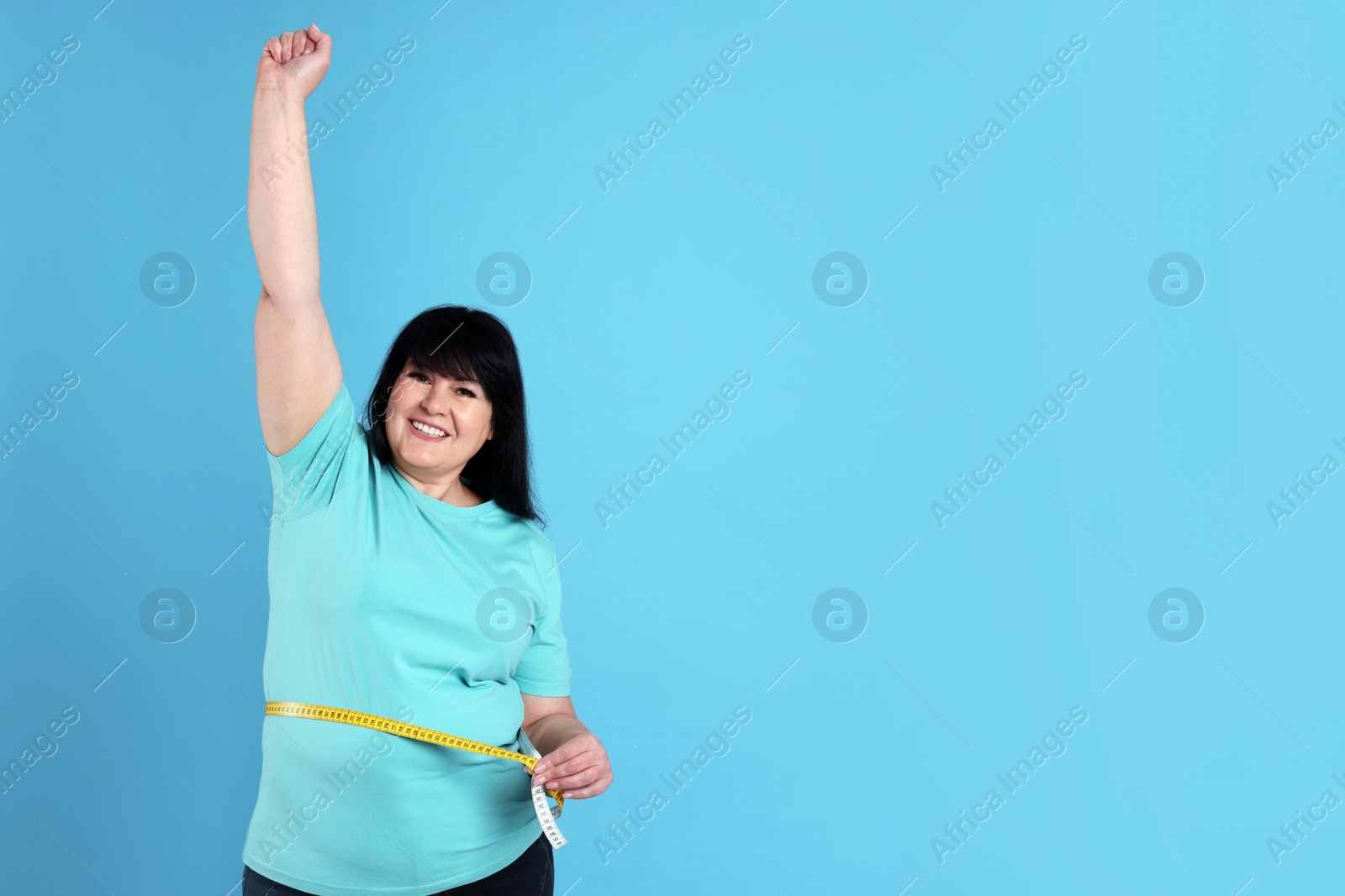 Photo of Happy overweight mature woman measuring waist with tape on light blue background, space for text