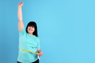 Happy overweight mature woman measuring waist with tape on light blue background, space for text