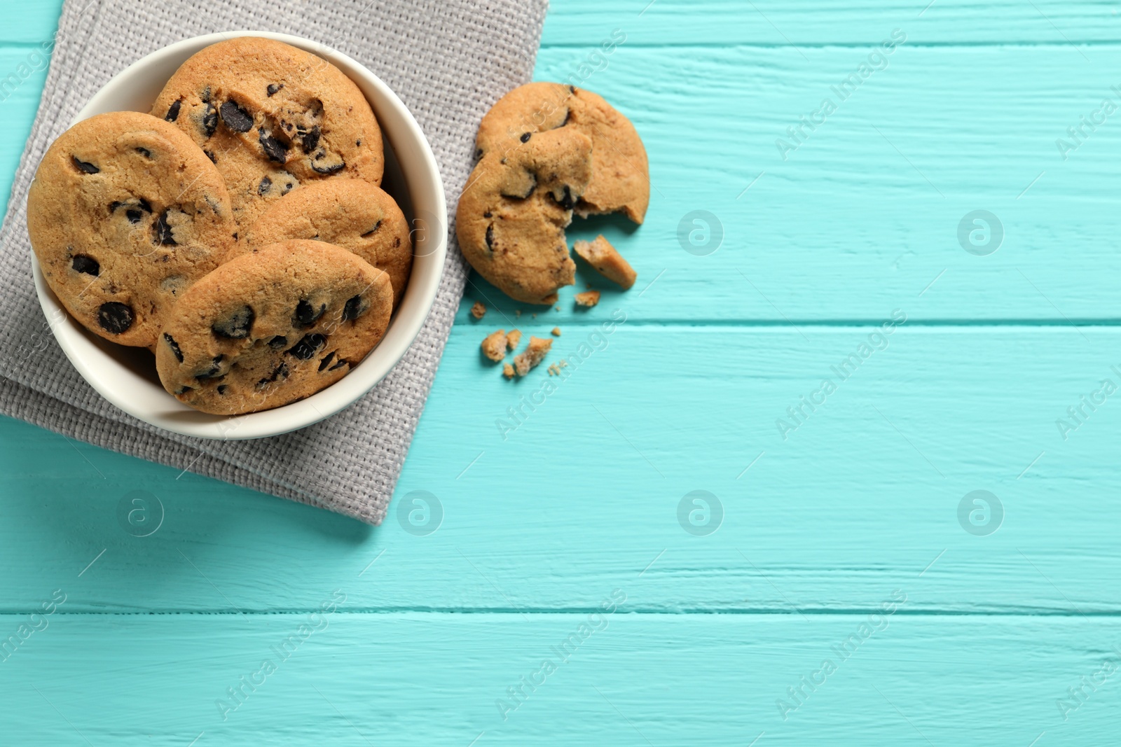 Photo of Bowl with many delicious chocolate chip cookies on turquoise wooden table, flat lay. Space for text