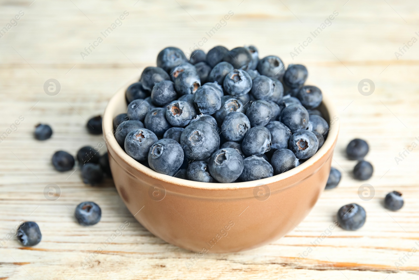 Photo of Tasty ripe blueberries in bowl on white wooden table