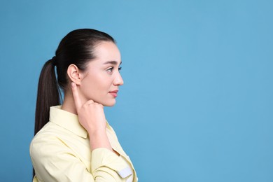 Young woman pointing at her ear on light blue background. Space for text