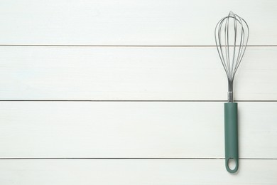 Photo of Metal whisk on white wooden table, top view. Space for text