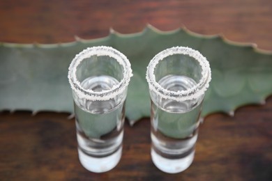 Photo of Mexican tequila shots with salt and green leaf on wooden table, closeup. Drink made of agava