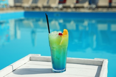 Refreshing cocktail on wooden table near swimming pool outdoors