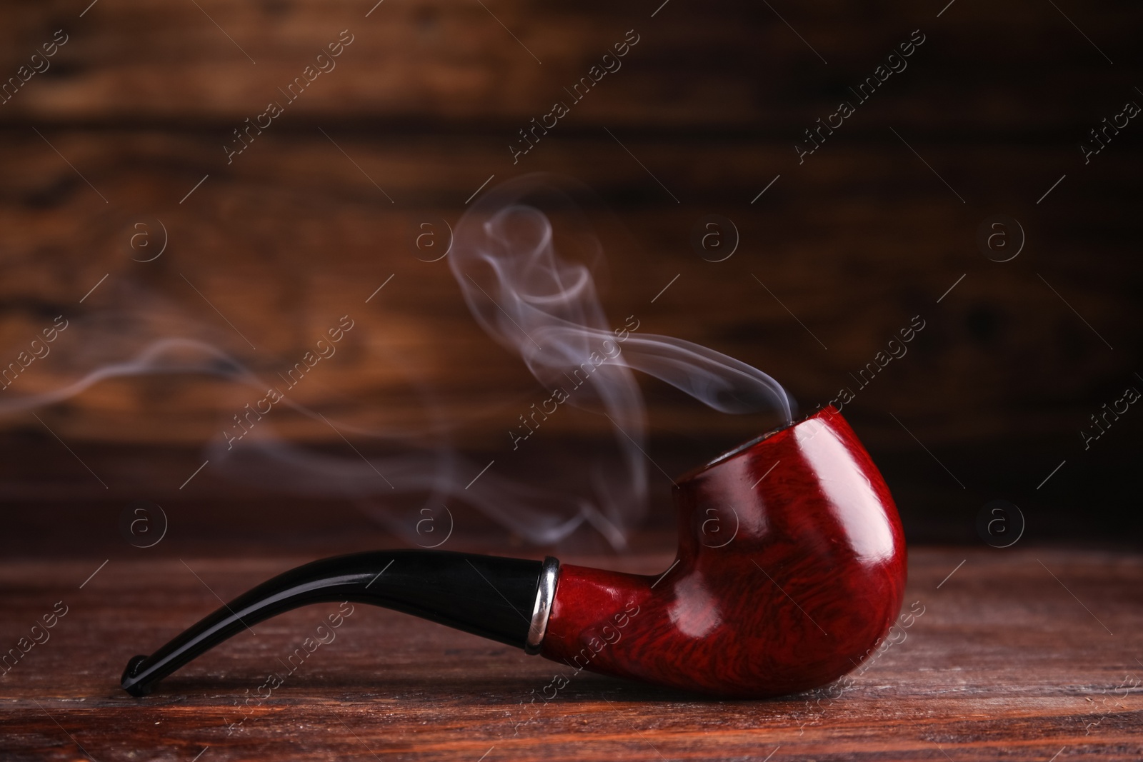 Photo of Stylish tobacco pipe with smoke on wooden table