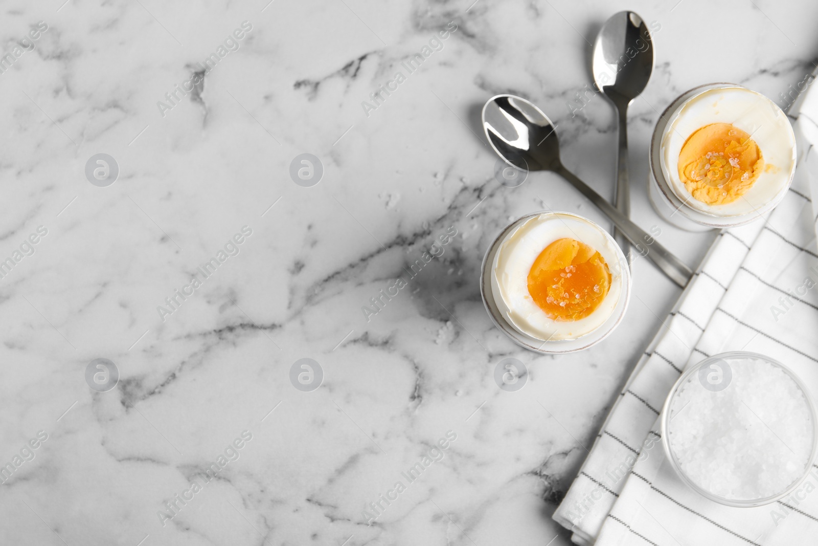 Photo of Tasty medium boiled eggs in ceramic holders on white marble table, flat lay. Space for text