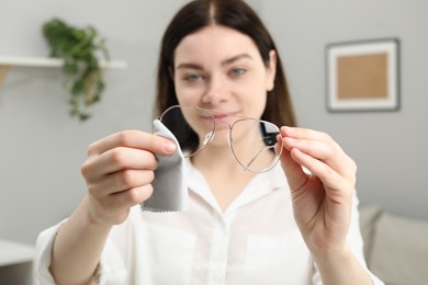 Photo of Beautiful woman cleaning glasses with microfiber cloth indoors, selective focus