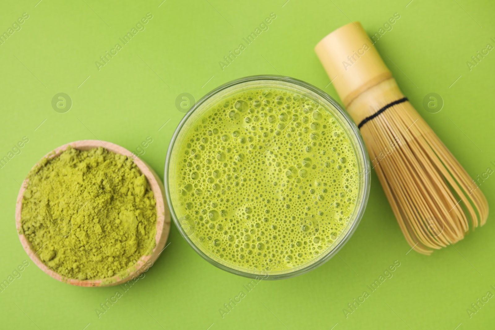 Photo of Glass of tasty matcha smoothie, powder and bamboo whisk on green background, flat lay