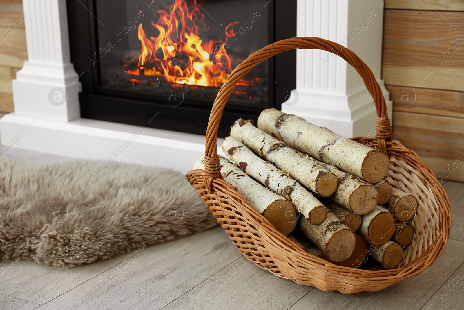 Photo of Firewood in wicker basket near burning fireplace indoors