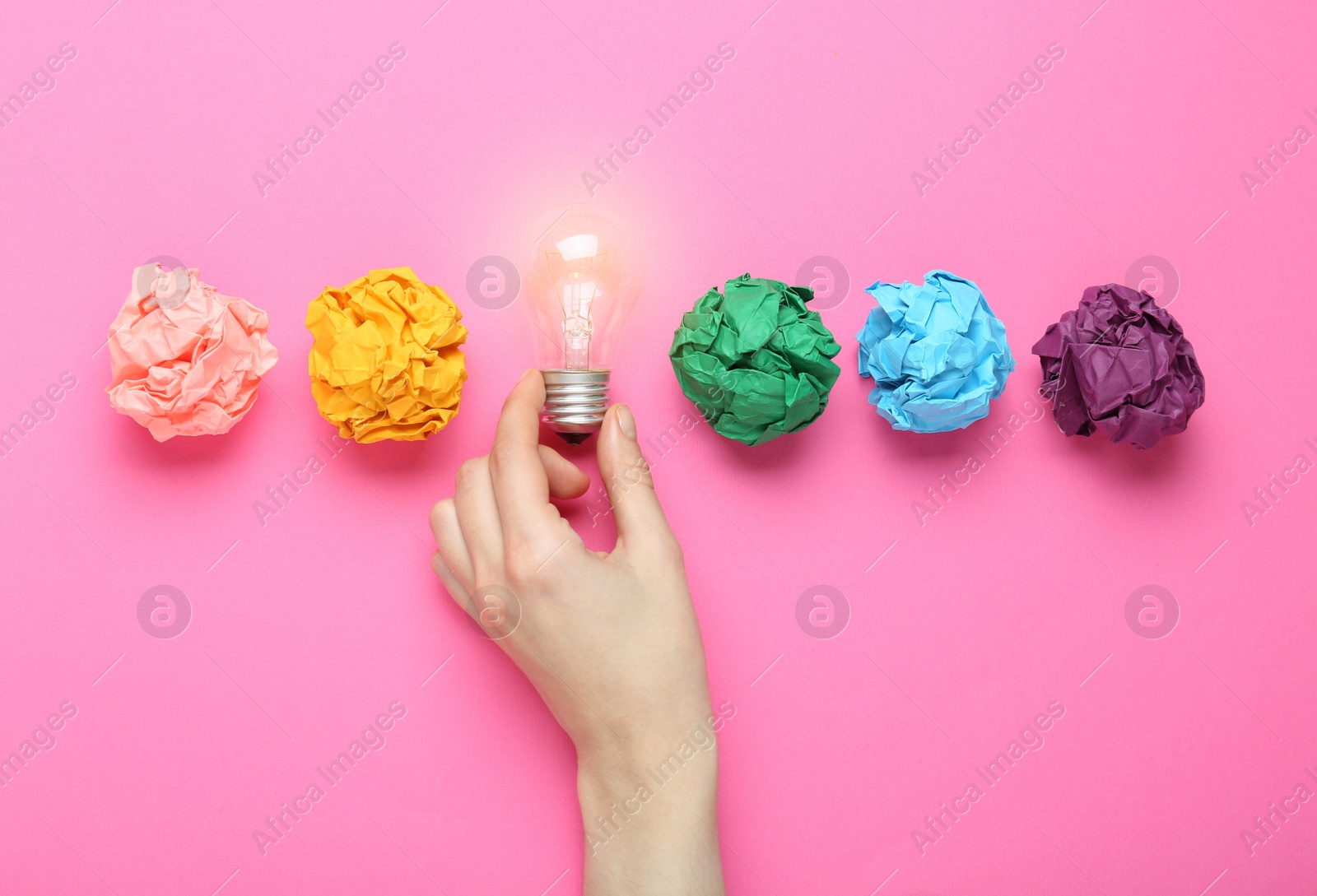 Photo of Woman holding lightbulb among colorful paper balls on pink background, top view. Idea concept