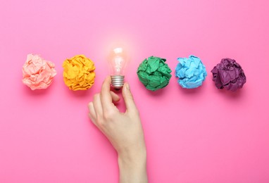 Photo of Woman holding lightbulb among colorful paper balls on pink background, top view. Idea concept