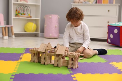 Photo of Little boy playing with wooden entry gate on puzzle mat in room. Child's toy