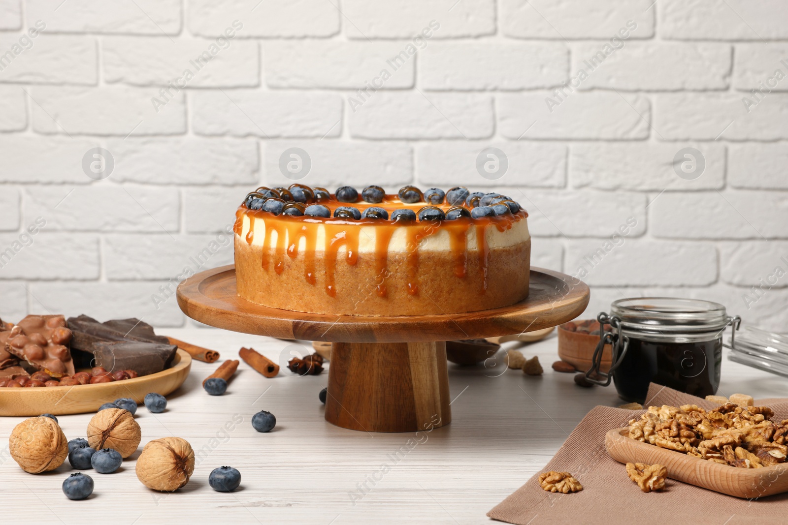 Photo of Delicious cheesecake with caramel and blueberries on white wooden table near brick wall