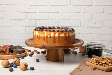 Delicious cheesecake with caramel and blueberries on white wooden table near brick wall