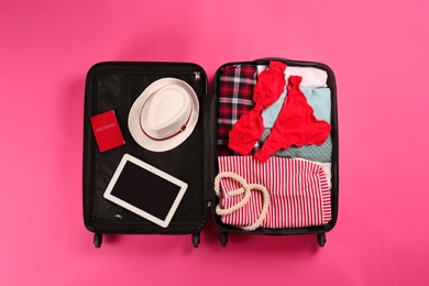 Photo of Open suitcase with traveler's belongings on color background, top view