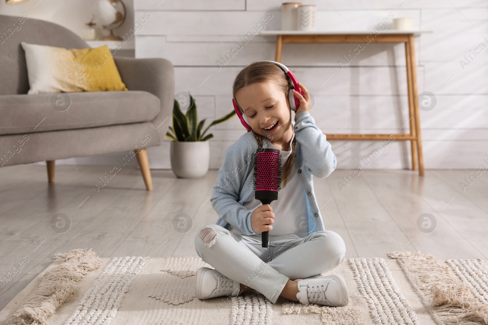 Photo of Cute little girl in headphones with hairbrush singing at home