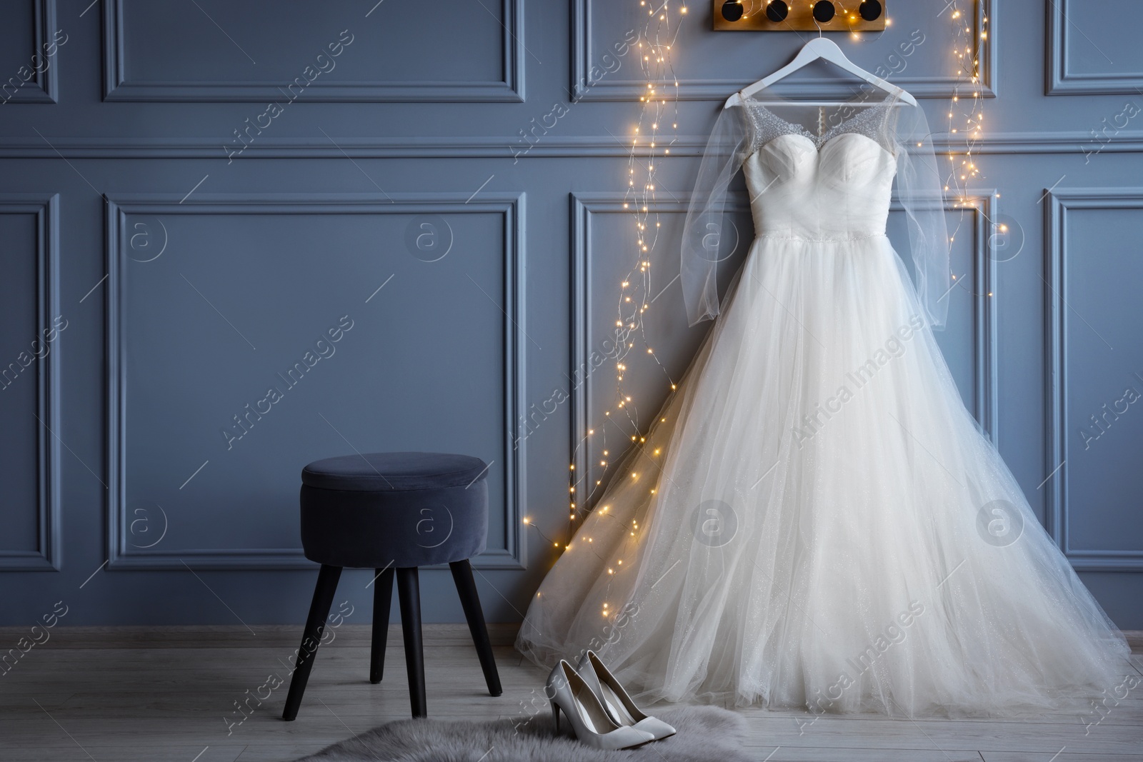 Photo of Fashionable long dress with transparent sleeves on hanger near festive lights and shoes in showroom. Preparing for party