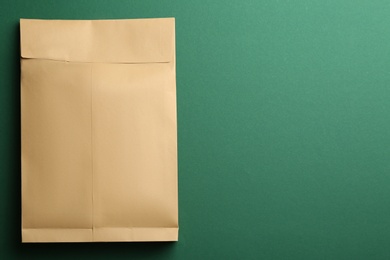 Kraft paper envelope on green background, top view. Space for text