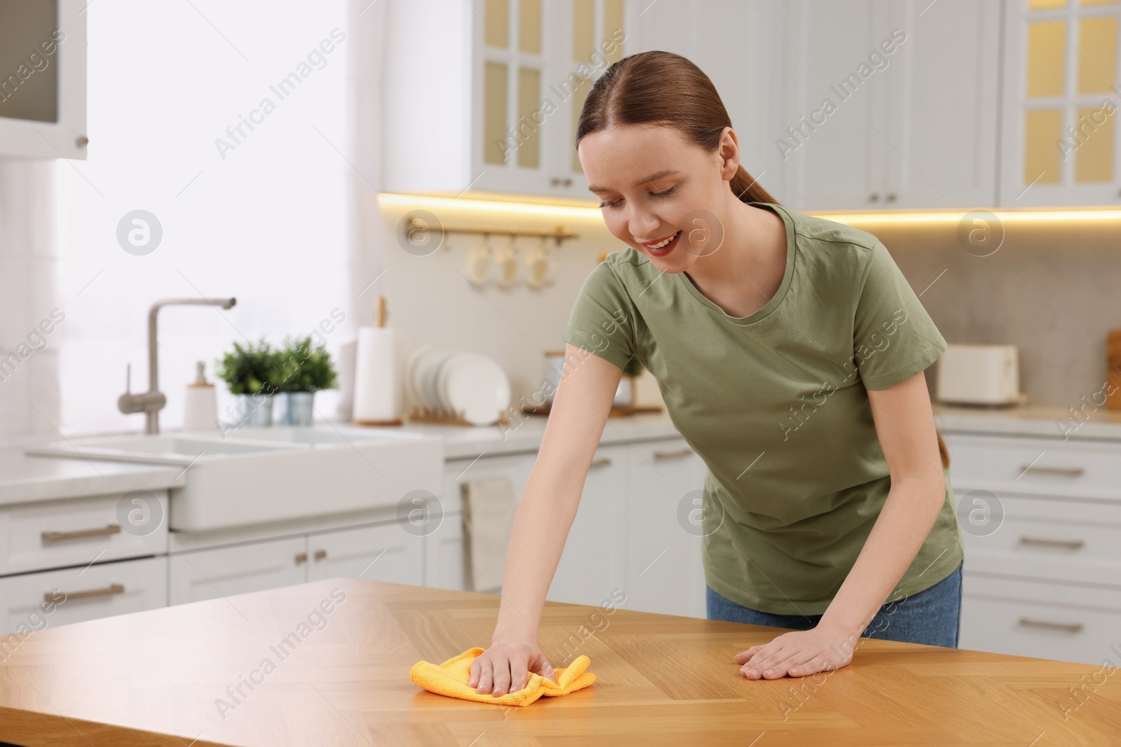 Photo of Woman with microfiber cloth cleaning wooden table in kitchen