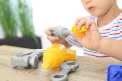 Little boy playing with toy construction tools at wooden table, closeup