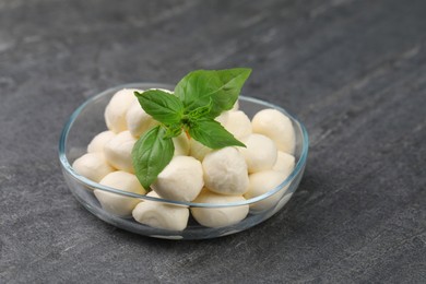 Tasty mozzarella balls and basil leaves in bowl on grey table