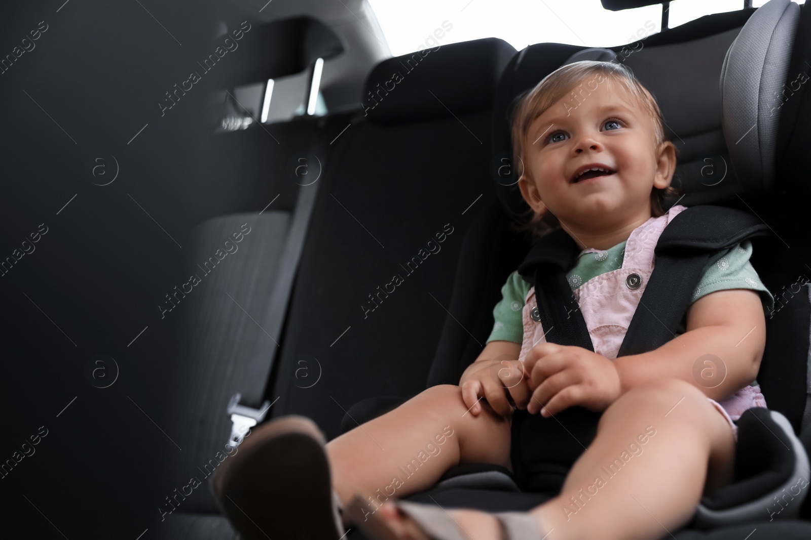 Photo of Cute little girl sitting in child safety seat inside car