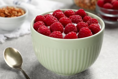 Photo of Bowl with delicious yogurt and raspberries on grey table, closeup