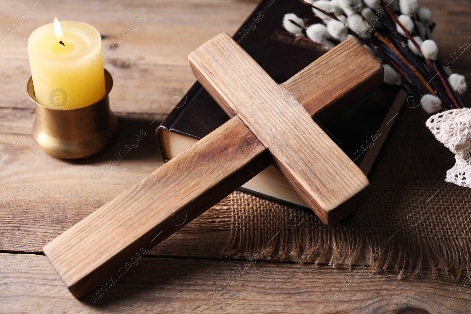 Photo of Cross, Bible, burning church candle and willow branches on wooden table, closeup