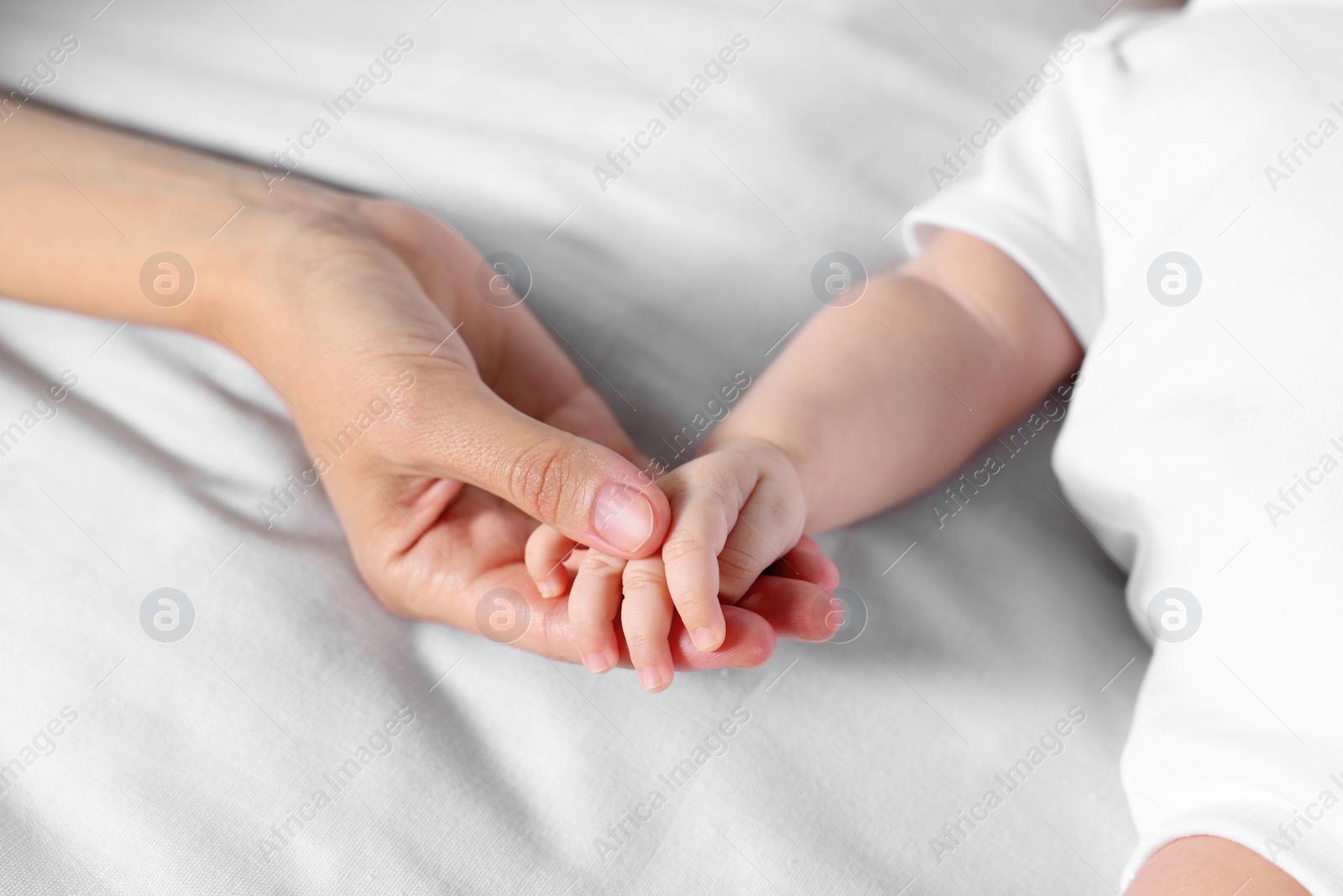 Photo of Mother holding hand of her little baby on bed, closeup