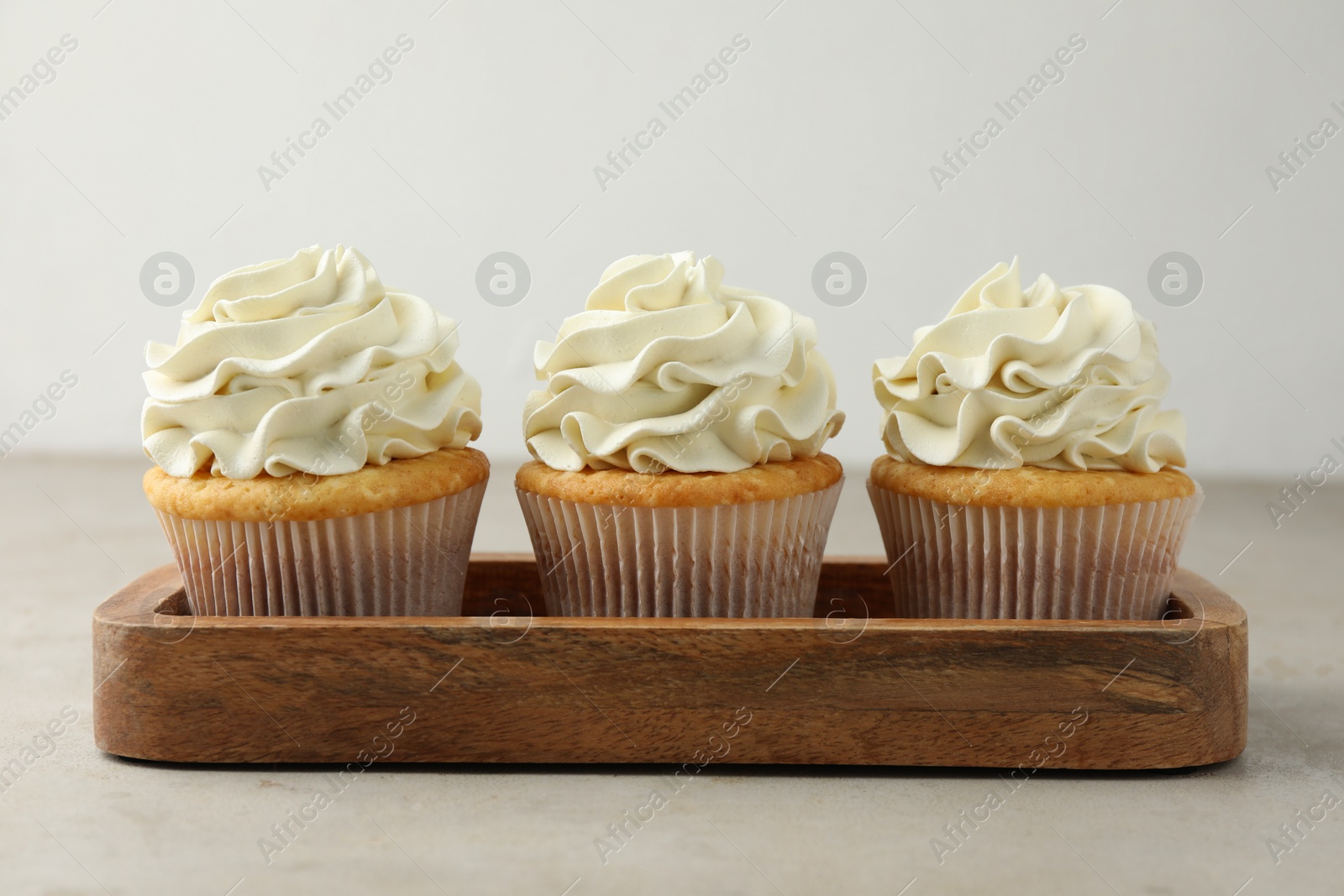 Photo of Tasty cupcakes with vanilla cream on light grey table, closeup